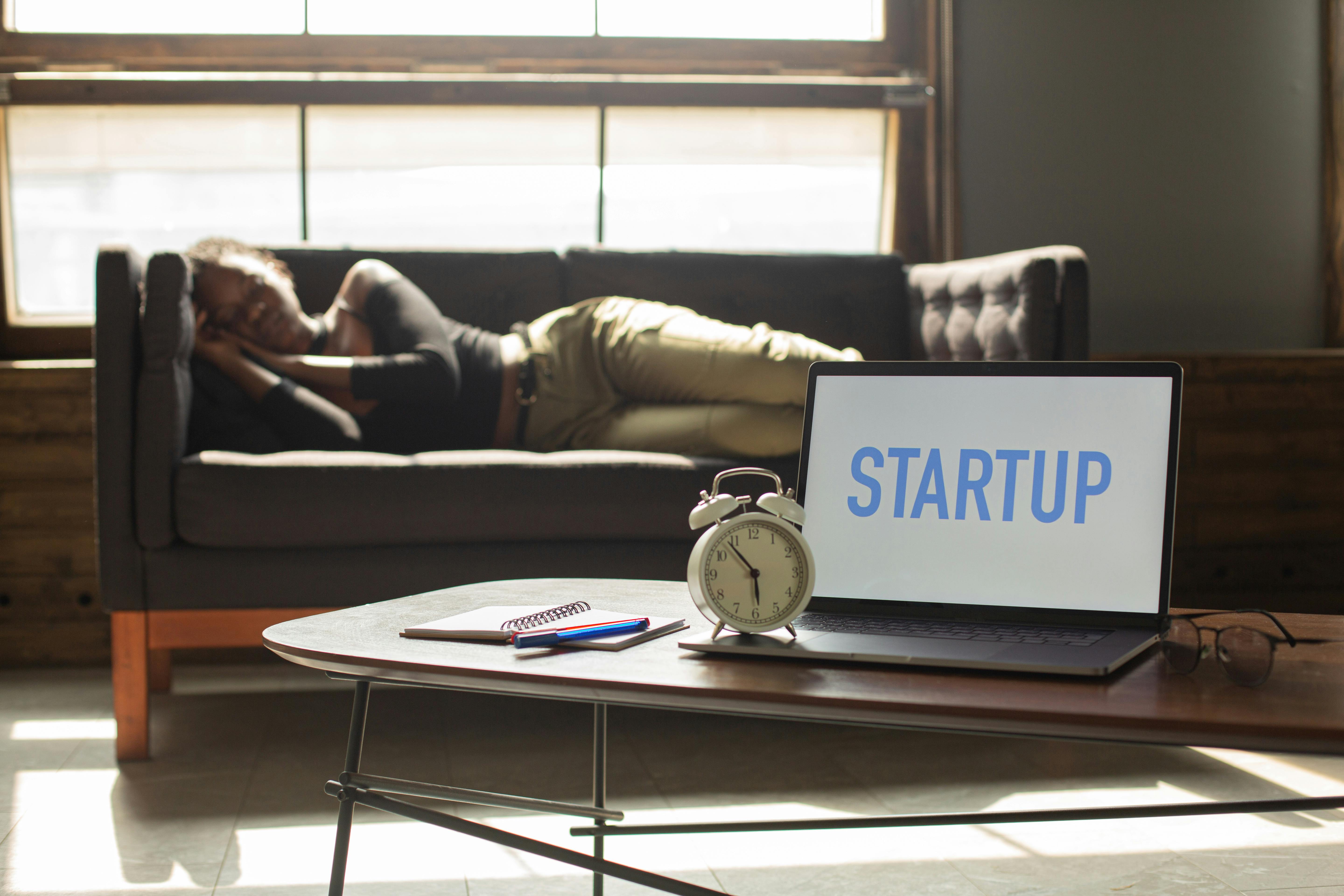 man napping on couch with computer showing the text "startup"