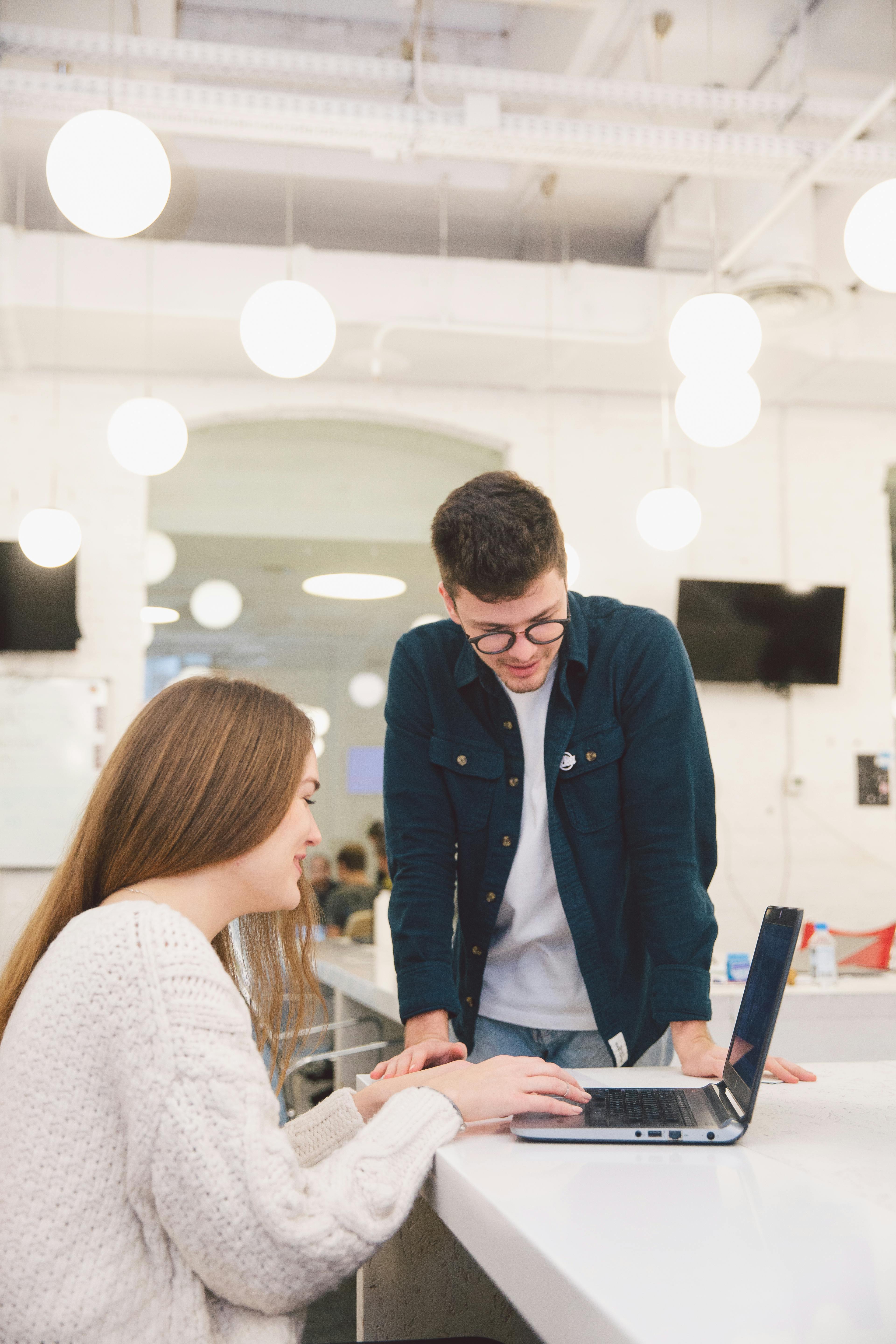 woman at laptop at desk with man in jacket standing next to her