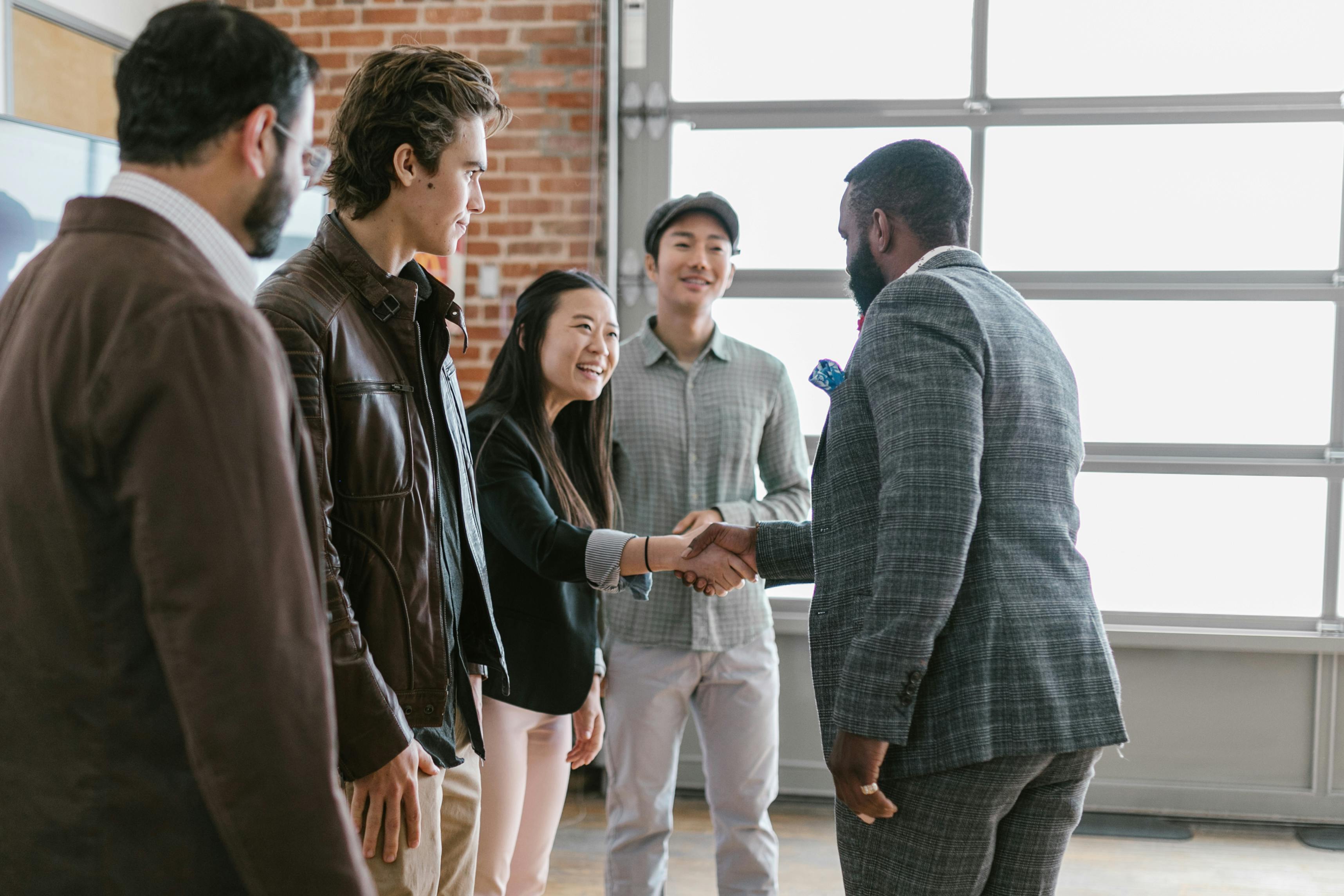 A group of four people in business attire with a man in front of them shaking the hand of someone in the group