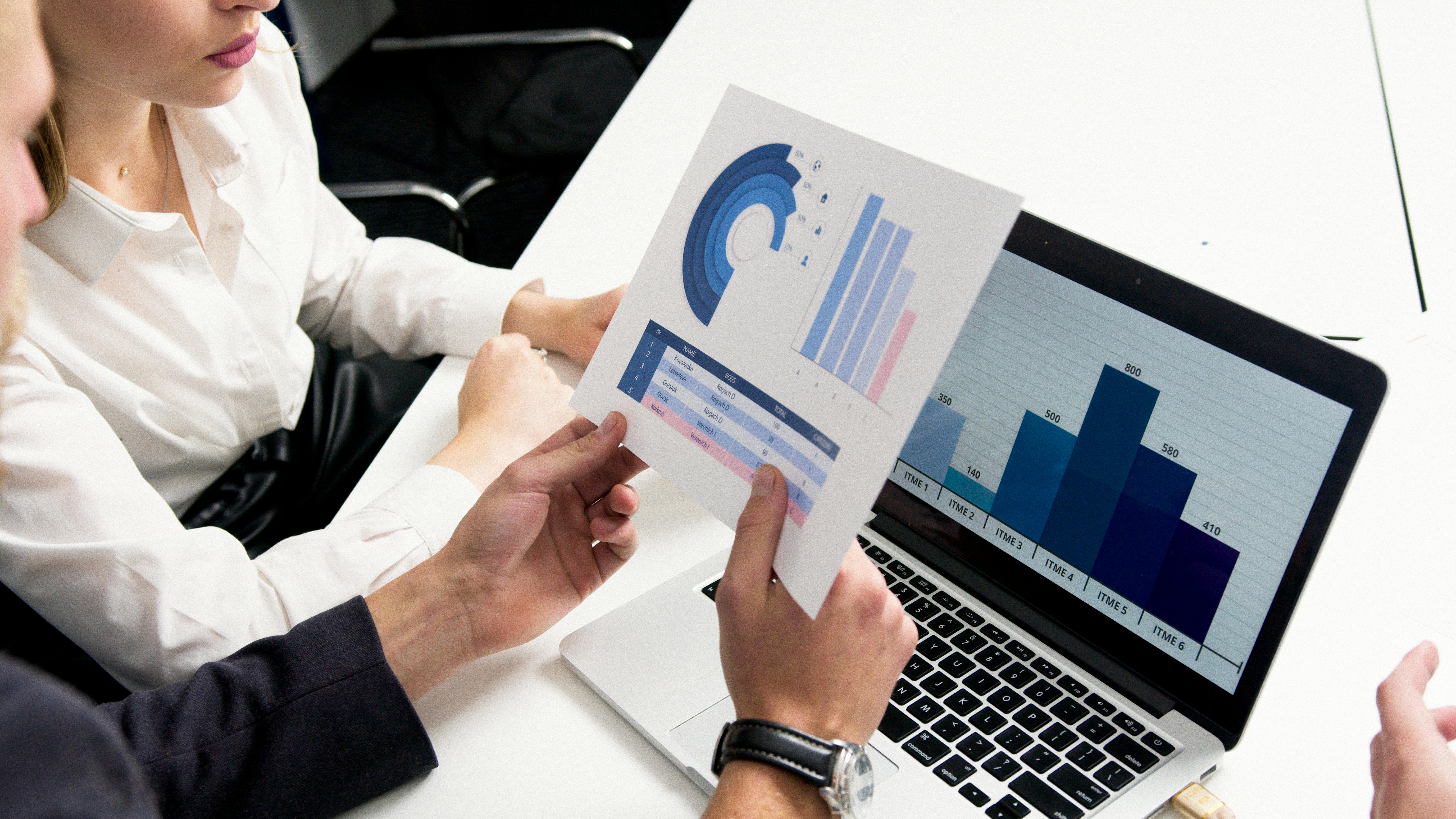 laptop with charts in front of man with paper chart