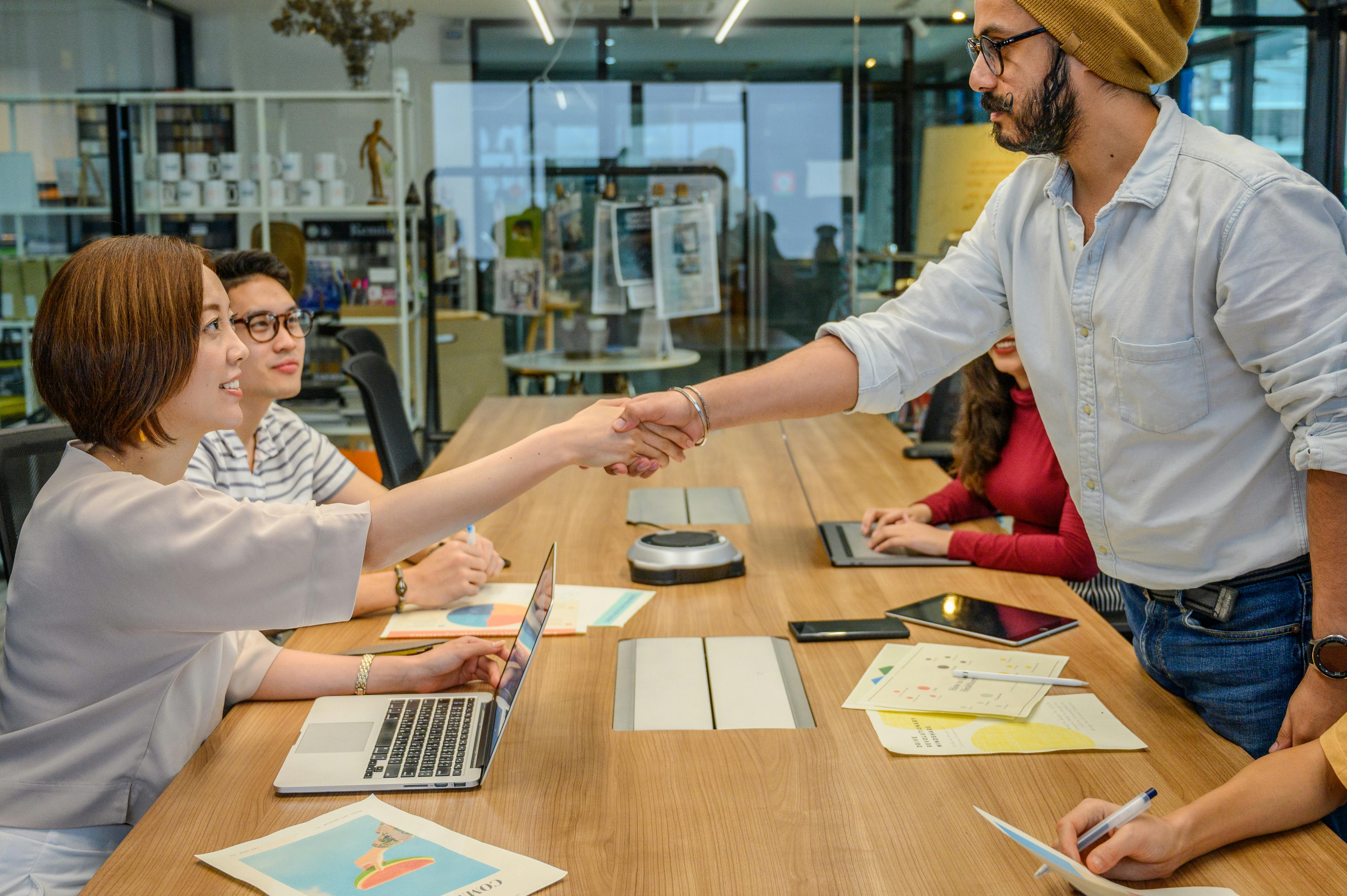 Three employees around table, with two shaking hands