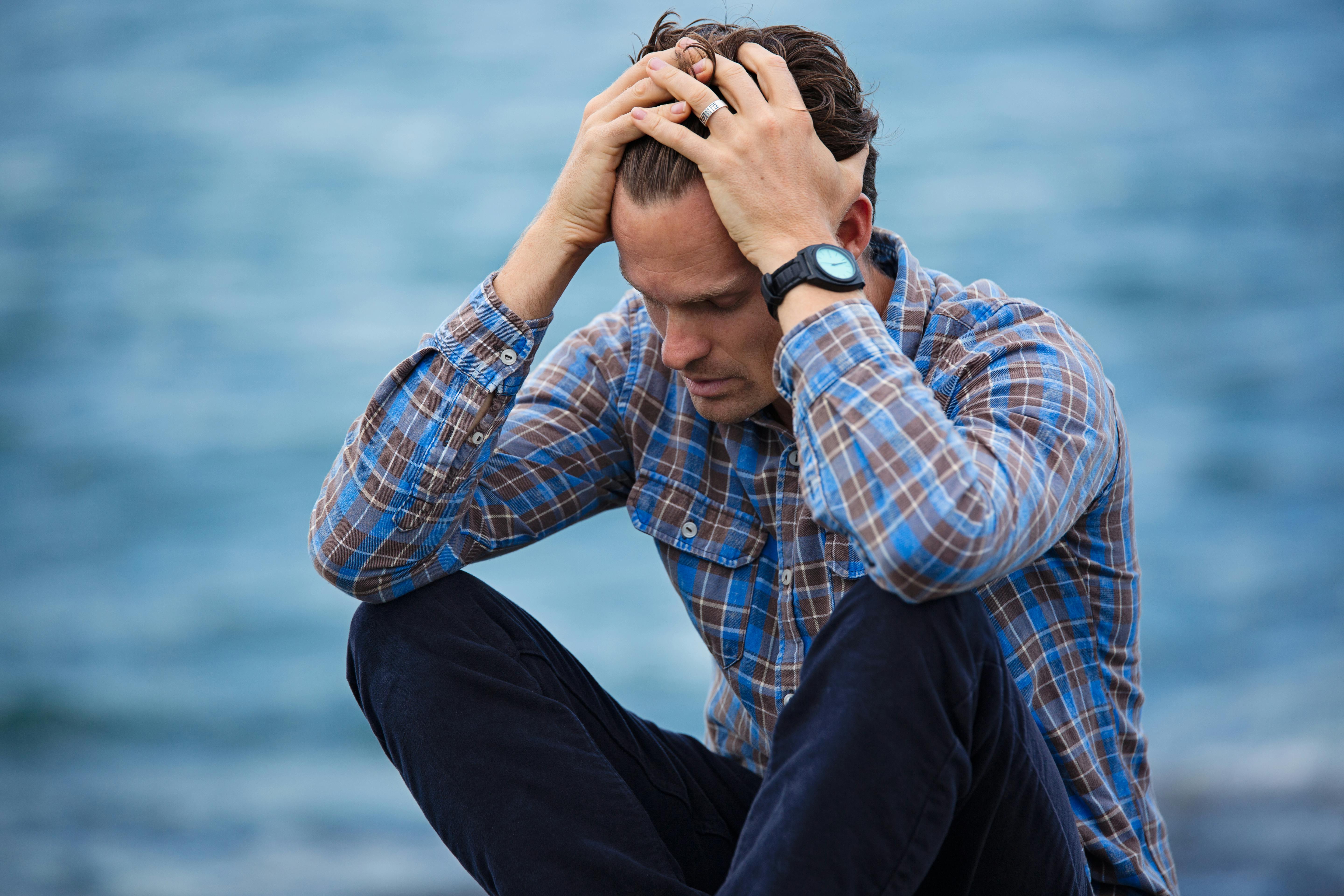 Man sitting by the water, stressed.