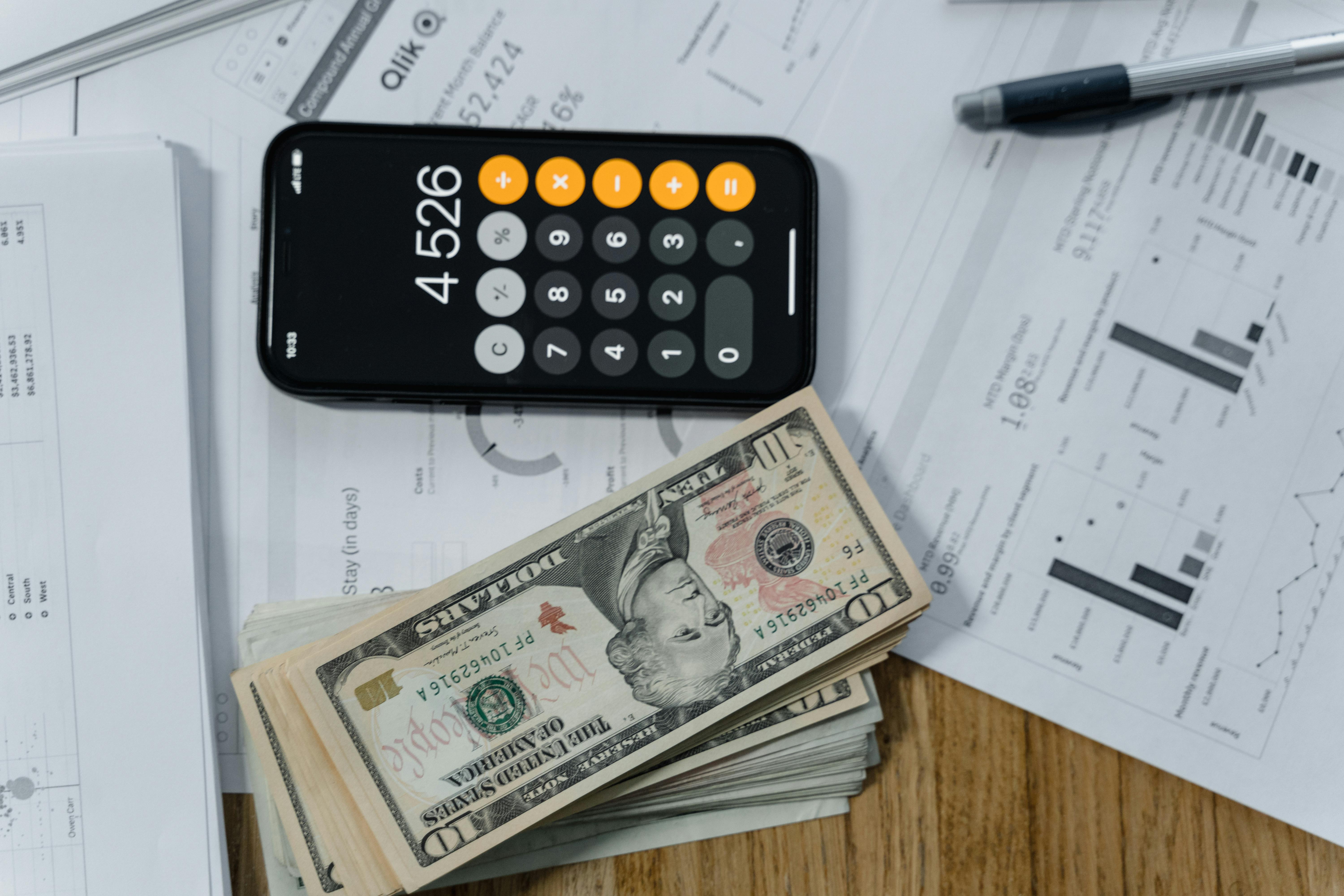 iPhone calculator on desk with stacks on 100 bills