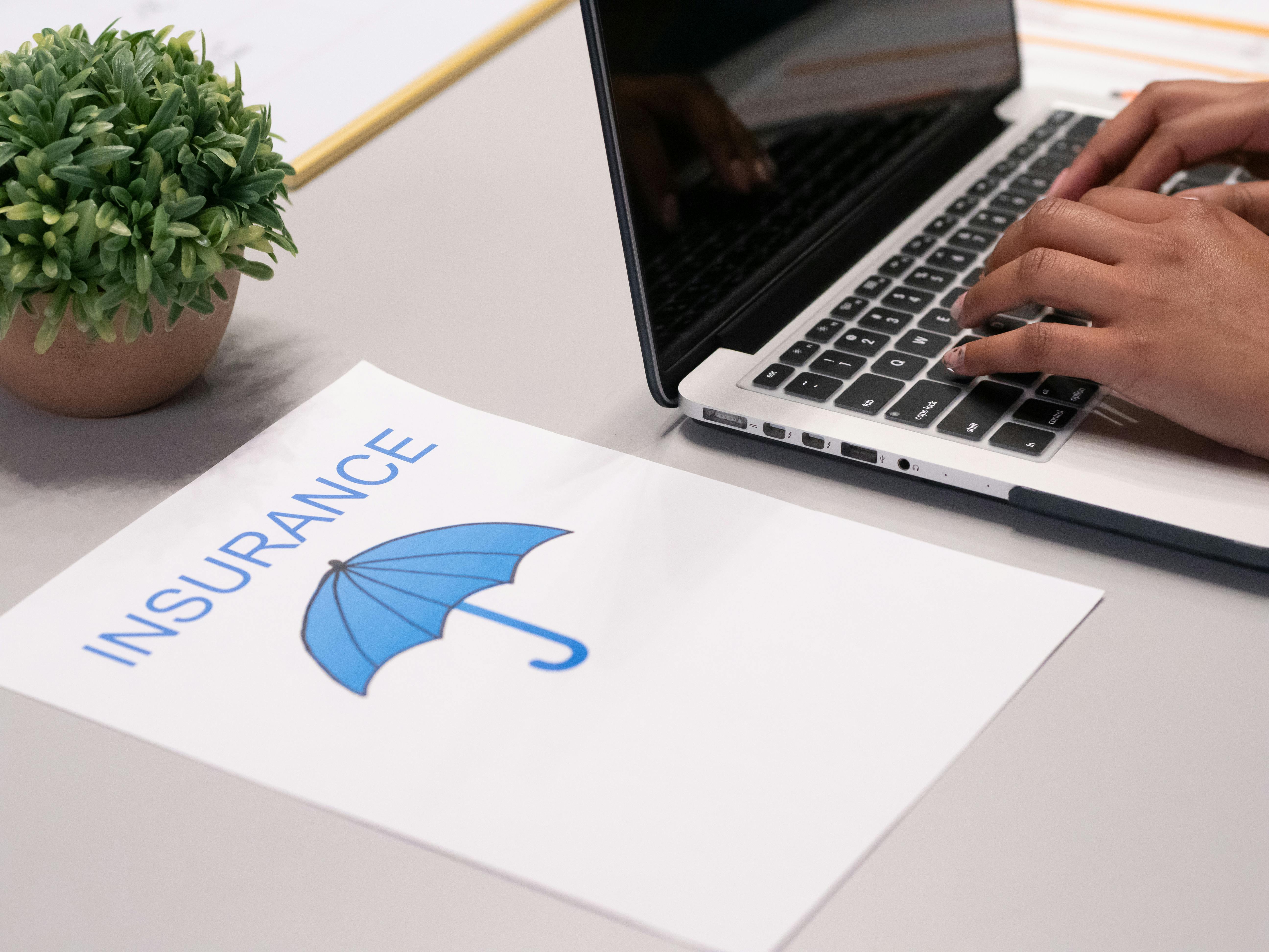 laptop and paper with "Insurance" and an umbrella