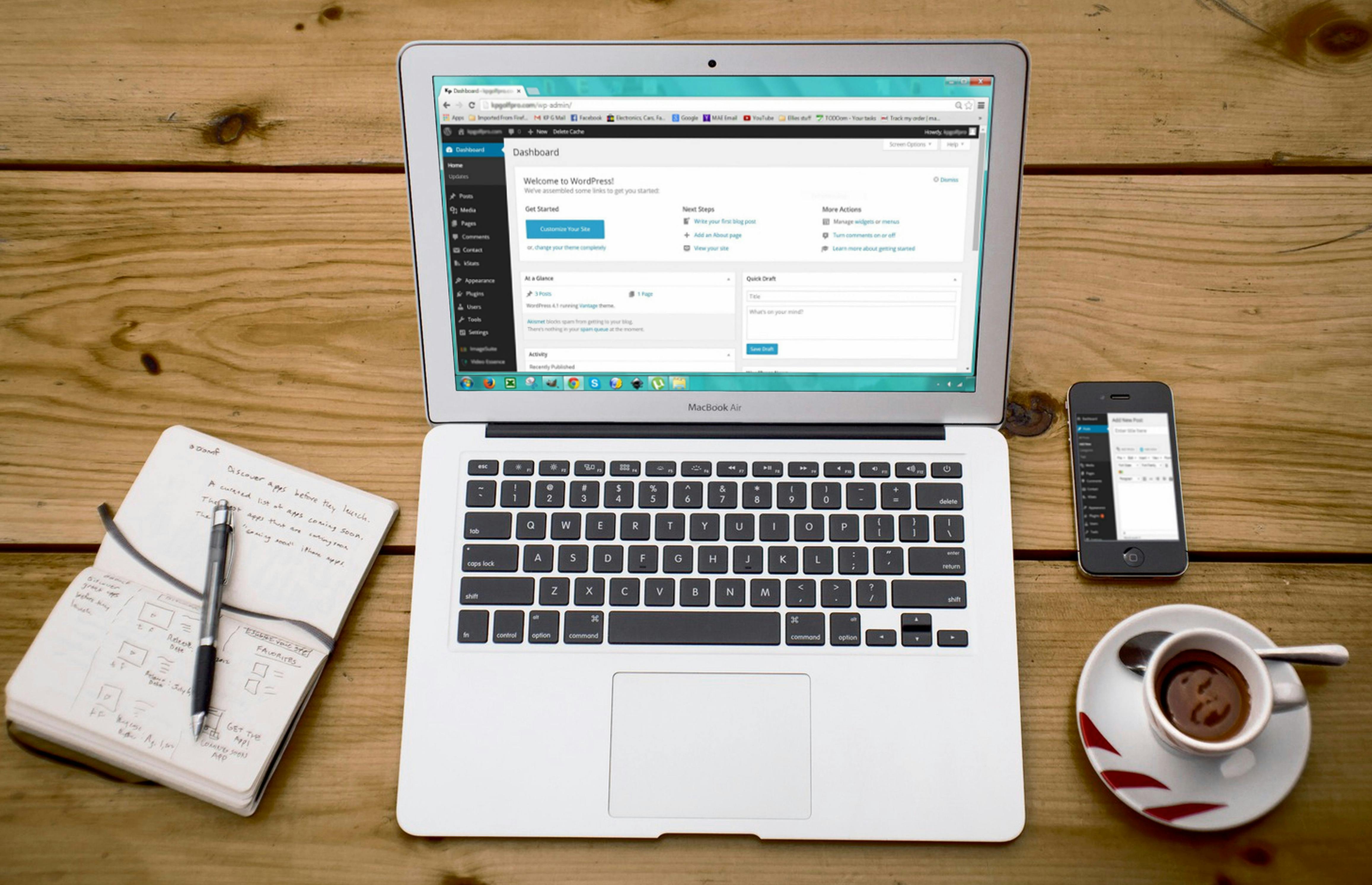 laptop showing wordpress on table with coffee, pen, and paper