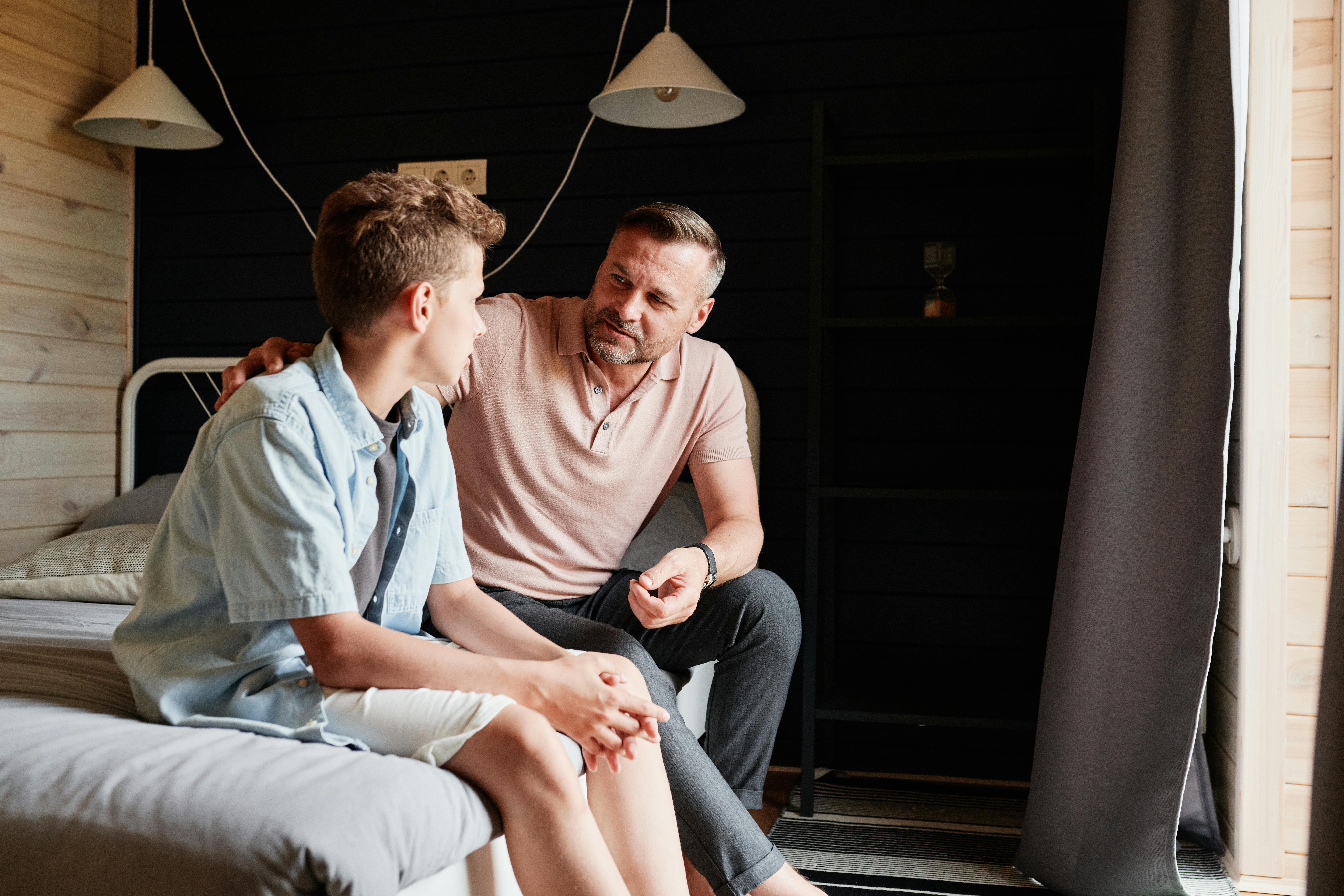 Father and son sitting on bed talking